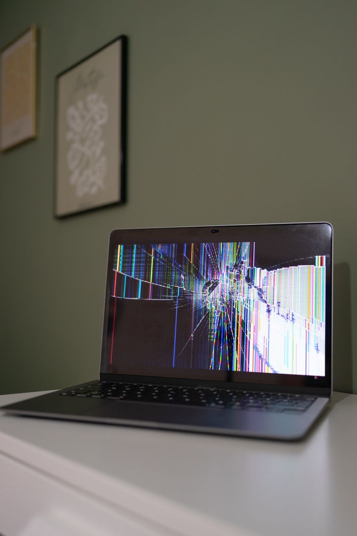 Home A laptop with a cracked and malfunctioning screen displayed on a desk indoors.