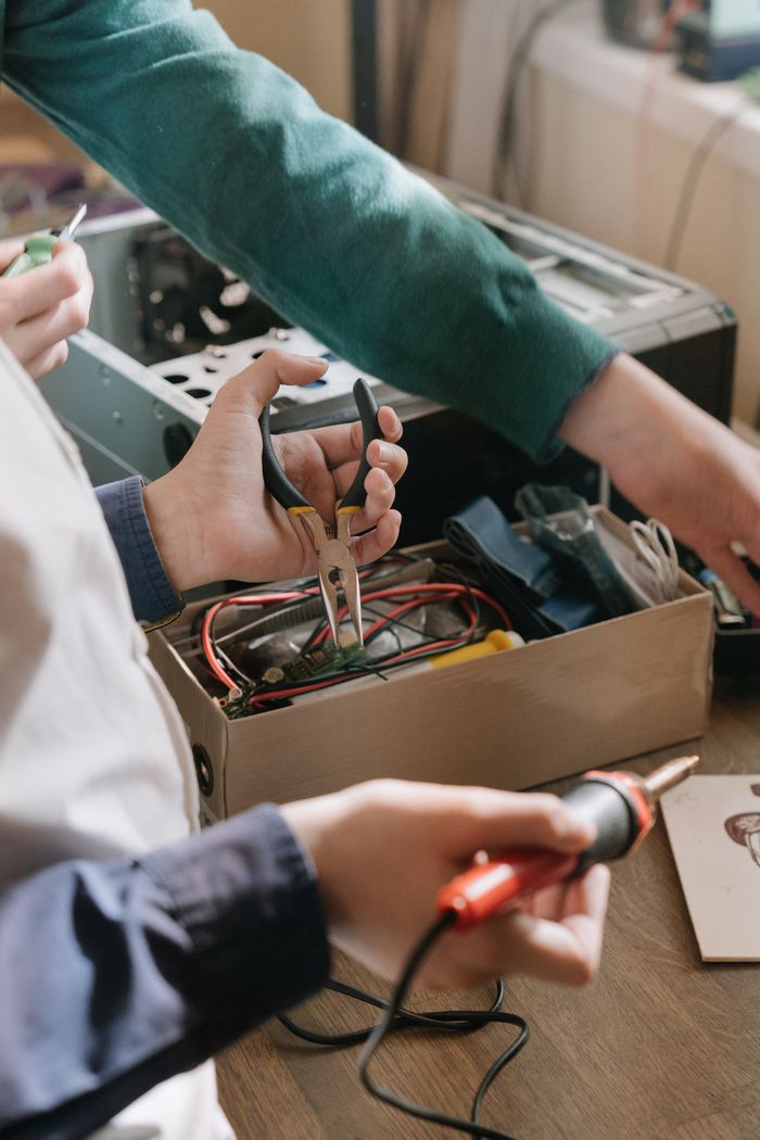 Offerings Close-up of hands repairing electronic device using soldering iron and pliers.