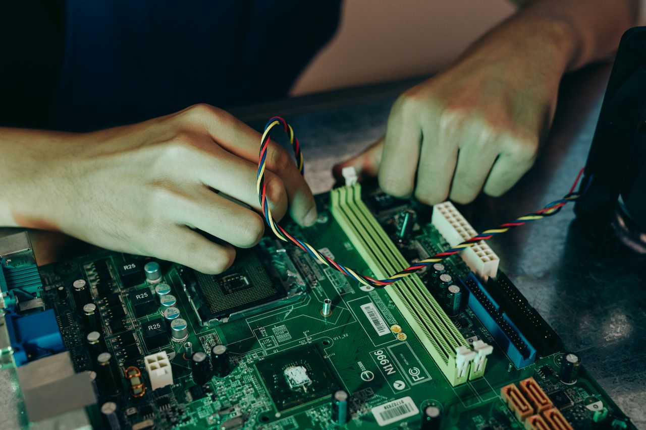 Home Person assembling computer motherboard with colorful wires, showcasing technology and engineering.